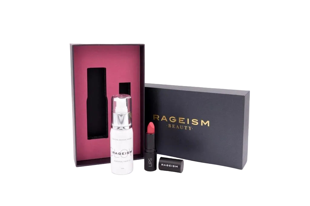 A beauty gift set from Rageism Beauty on a white background, featuring a white serum bottle, a red lipstick, and a black lipstick case, displayed alongside a dark pink inner box and a black outer box with gold lettering.